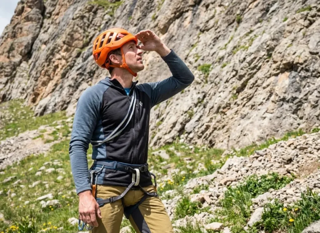 Helmeted climber scanning route above for loose rock and environmental hazards