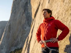 Why Free Soloing Is Not Just Climbing Without Ropes A professional climber in a red Arc'teryx jacket looking up at the base of El Capitan in Yosemite, illuminated by golden hour sunlight.