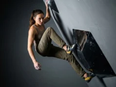 Grip Dual-Texture Holds Without Slipping Off A professional climber wearing Arc'teryx gear and La Sportiva shoes carefully placing a foot on a glossy black dual-texture bouldering volume in a dimly lit climbing gym.