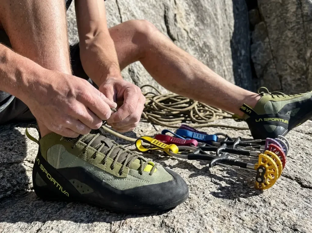 A climber lacing up La Sportiva TC Pro shoes at the base of El Capitan with a Camalot rack nearby