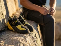 Keep The Downturn In Your Shoes For Longer Close-up of La Sportiva Solution climbing shoes resting on a granite boulder at sunset, highlighting the aggressive downturned shape and pristine yellow rubber tension system.