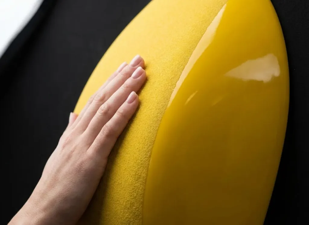 Macro close-up of a climber's hand pressing on a dual-texture climbing hold, highlighting the contrast between the rough friction zone and the glossy, slippery surface.