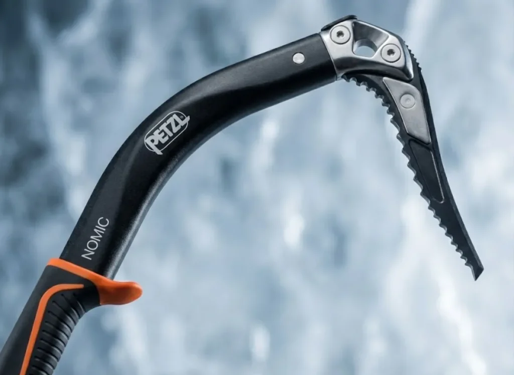 Close-up macro photography of a Petzl Nomic ice tool head, highlighting the offset handle geometry and machined steel pick weights.