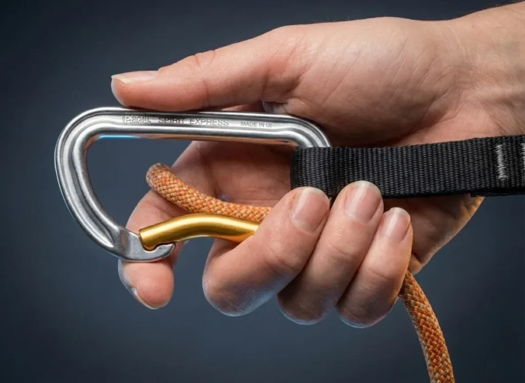 Macro close-up of a climber's hand performing the pinch clipping technique on a Petzl quickdraw, highlighting the finger positioning and gear texture.