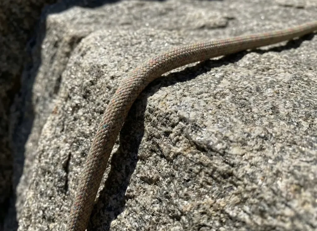 Close-up of a climbing rope dragging over a rock edge, illustrating the friction mechanics described by the Capstan Equation.