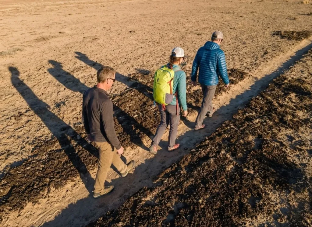 Three climbers walking single file across desert approach to minimize cryptobiotic soil damage