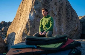Stack Pads To Eliminate Gaps In Landing Zones A professional climber stands confidently on a meticulously stacked system of Organic Climbing and Black Diamond crash pads at the base of a highball boulder during sunset in the Buttermilks.
