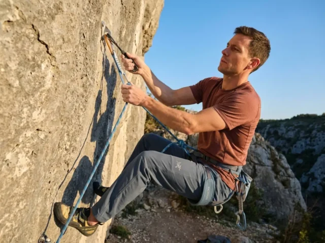 stick-clip-first-bolt-ground-fall-prevention Climber using stick clip device to safely clip first bolt at 12 feet on outdoor sport climbing route