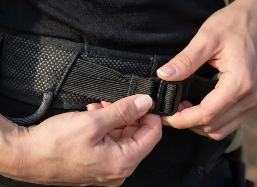 Macro photography of a climber's hands adjusting the rear elastic riser straps on a Black Diamond harness to customize the fit.