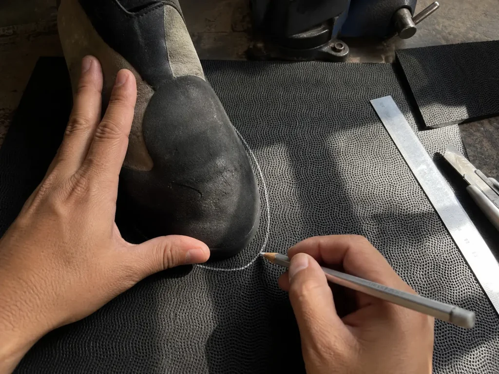 Hands marking a climbing shoe outline on a 4mm Vibram soling rubber sheet before cutting