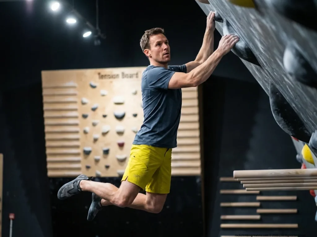Climber mid-4x4 power endurance training on overhang wall, feet cut, catching sloper — comp training block