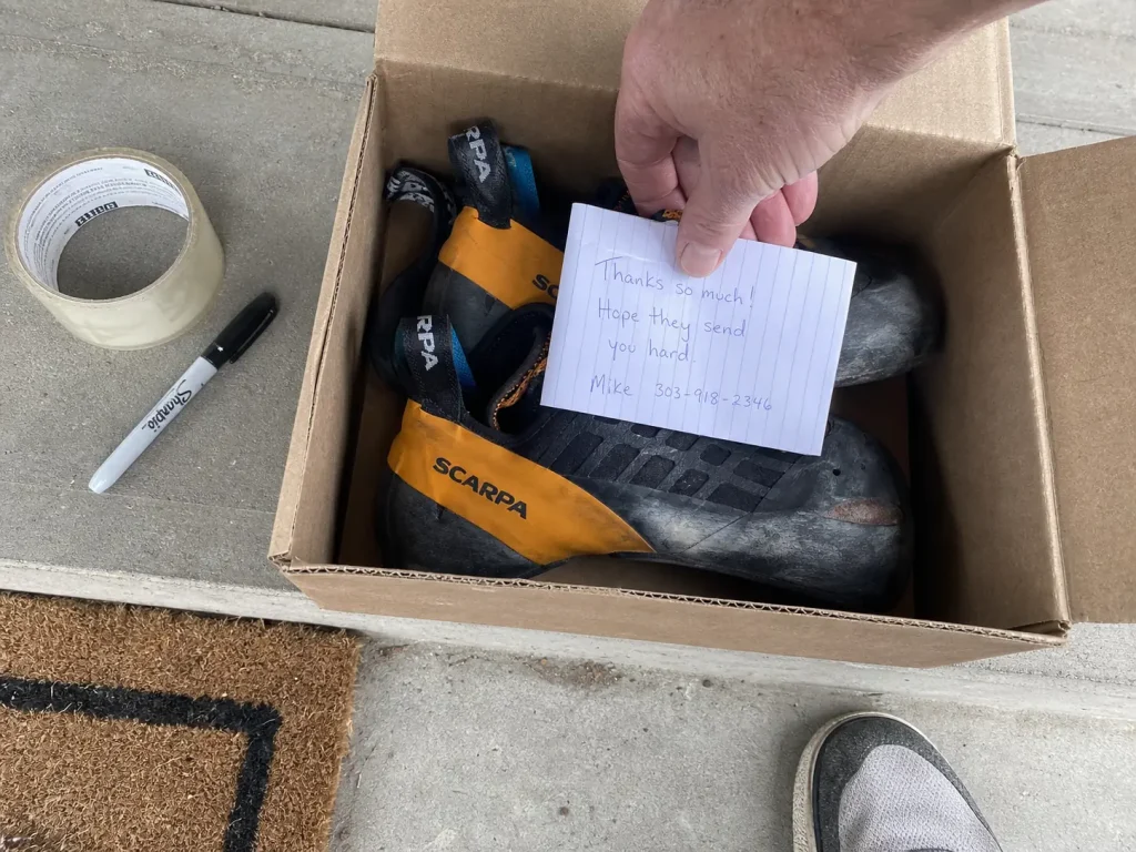 Packing worn climbing shoes into a shipping box with a note before mailing them to a resoler