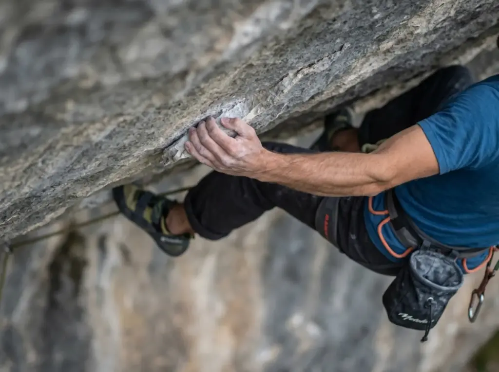 Climber applying full crimp grip on limestone edge showing tendon tension on fingers
