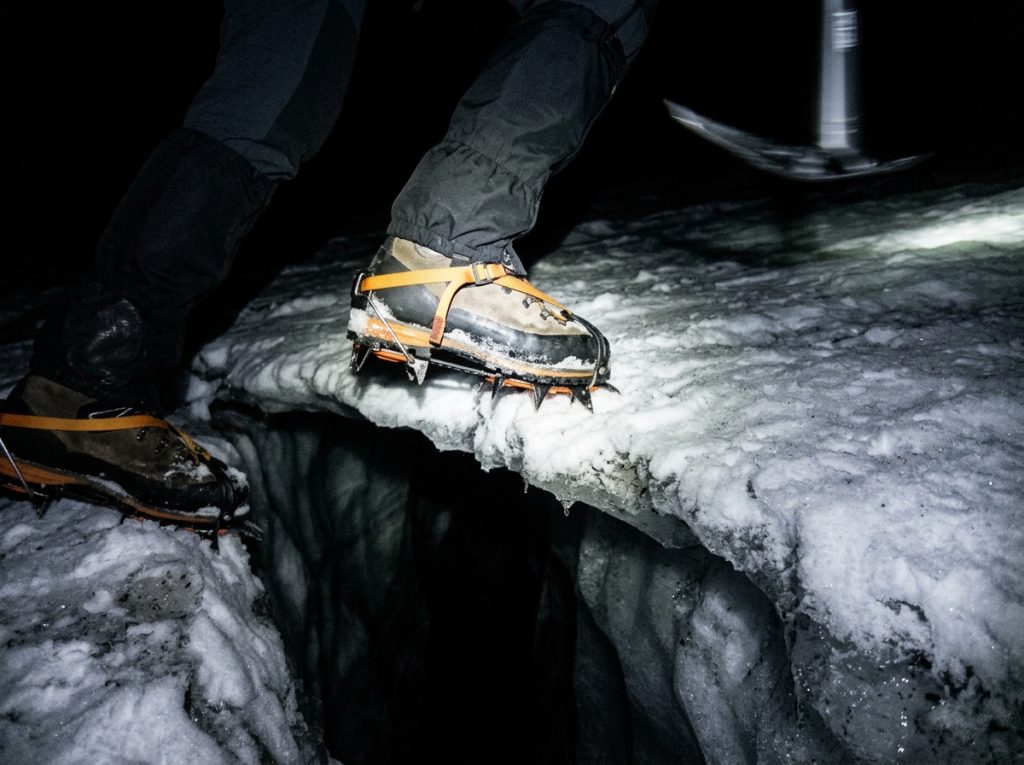 Climber stepping over a bergschrund gap on a firm early-season snow bridge