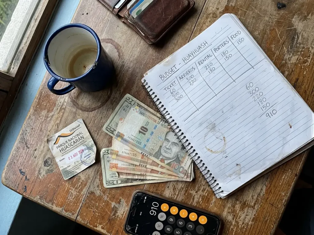 Peruvian soles, US dollars, a park ticket and a handwritten budget on a table for a Cordillera Blanca climb