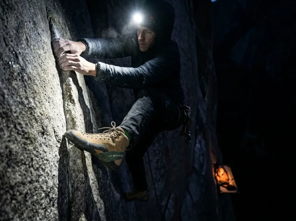 Climber edging by headlamp at night on El Capitan's Dawn Wall, a portaledge glowing in the dark below