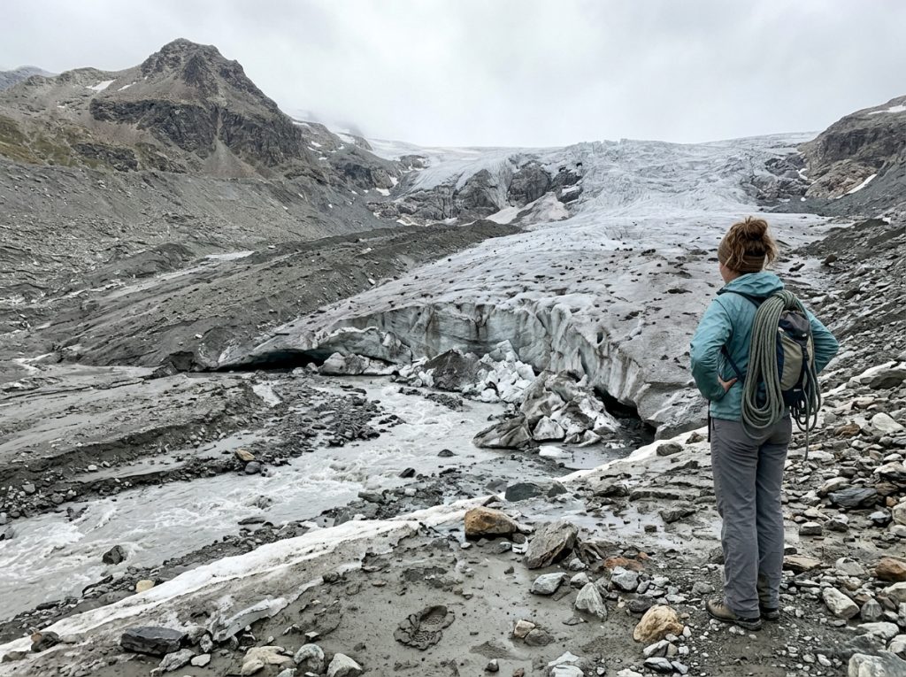 Climber studying a shrunken glacier snout and bare moraine where snow once covered rock