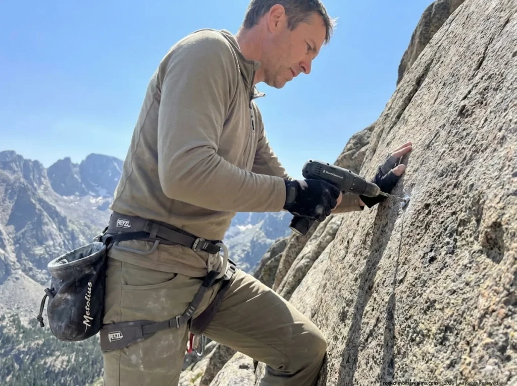 Climber hand-drilling a bolt in wilderness alpine terrain — PARC Act and legal fixed anchor placement