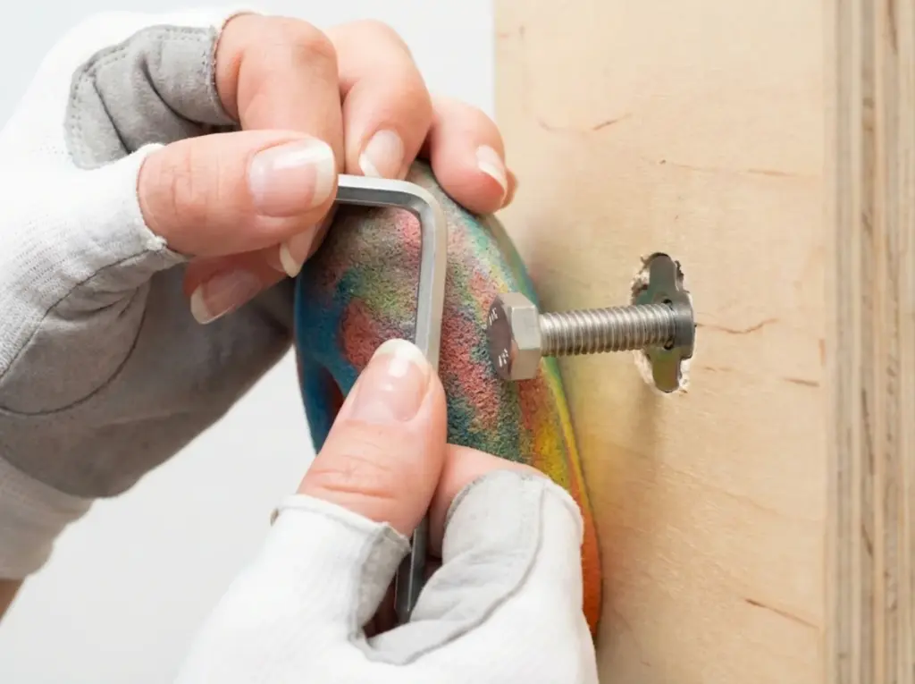 Hands tightening climbing hold bolt showing proper T-nut engagement on home wall