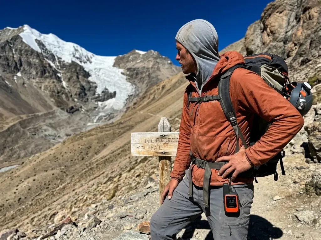 Solo climber with a Garmin inReach Mini 2 clipped to a pack strap at a remote Cordillera Blanca trail junction