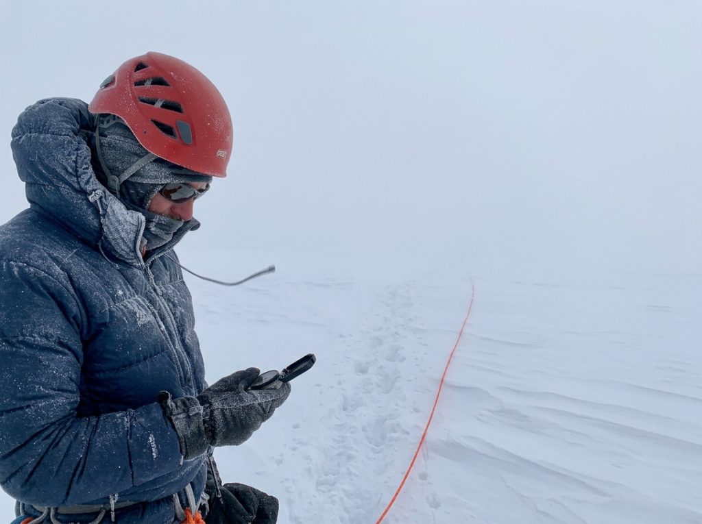 Climber navigating a whiteout on a featureless glaciated summit plateau