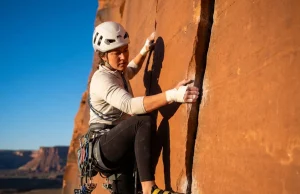 Read Any Crack and Place the Right Jam Every Time Climber placing a hand jam in a sandstone splitter crack at Indian Creek with tape gloves and cams on harness