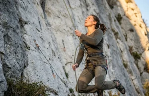 The Soft Catch Trick Most Belayers Get Wrong Belayer jumping to give a soft catch on a limestone sport route, Petzl GriGri, golden light