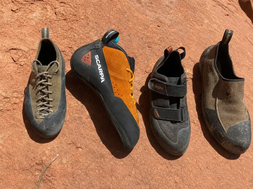 Four crack climbing shoes lined up on red sandstone showing flat lasts, stiff soles and high cuffs