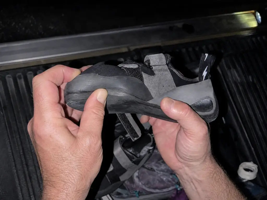 Hands flexing the worn toe of a crack climbing shoe to check the sole before a resole