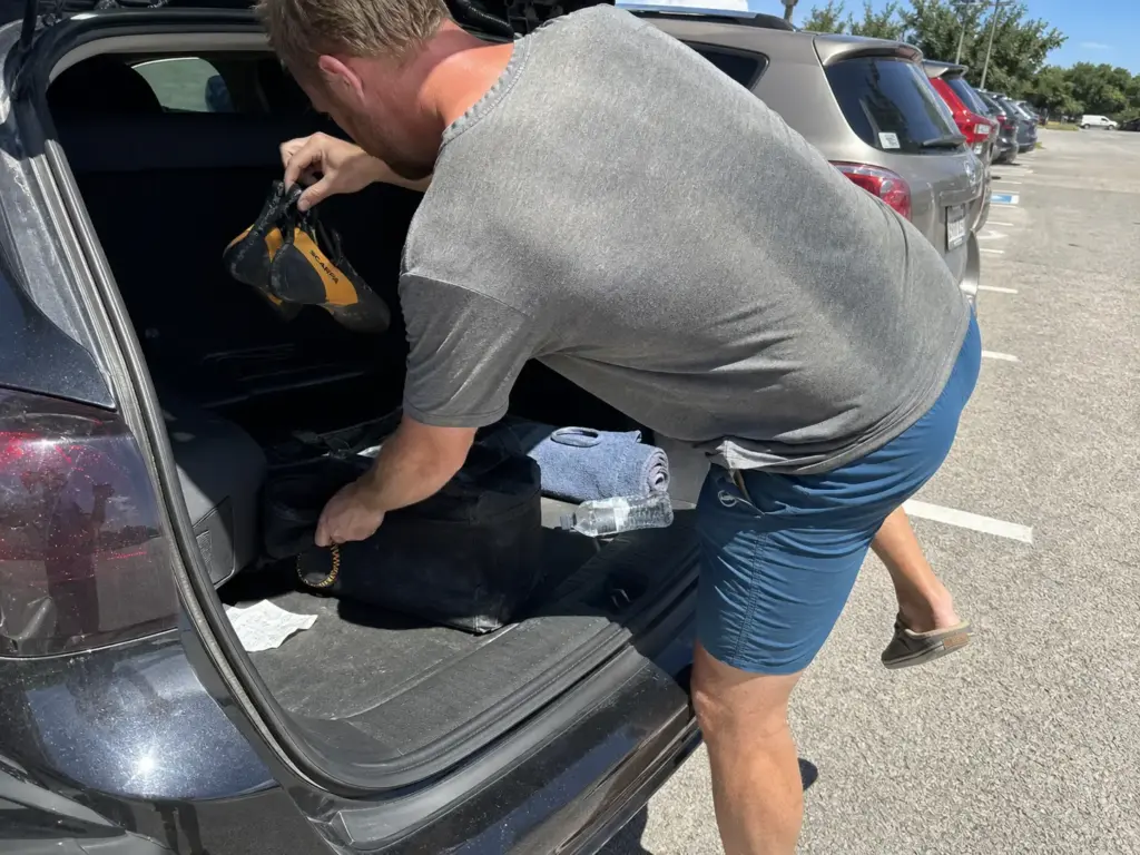 Climber lifting climbing shoes out of a hot car trunk, the storage habit behind most delamination