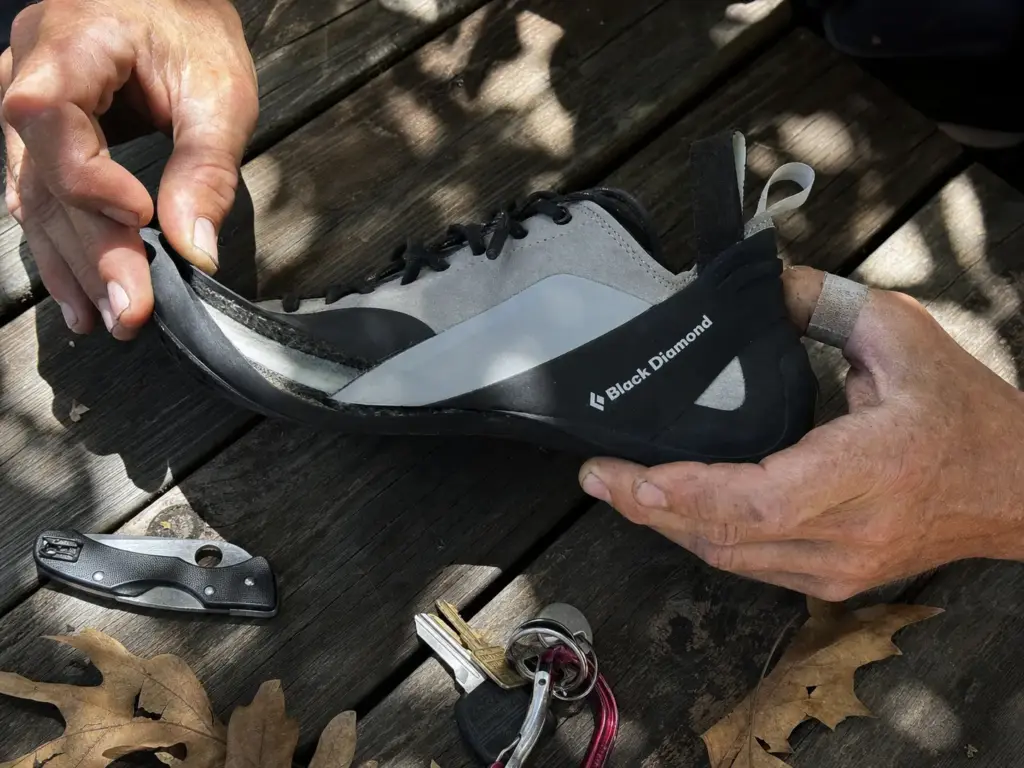 Close-up of a lifted climbing shoe rand exposing a rigid plastic midsole edge that glue cannot bond