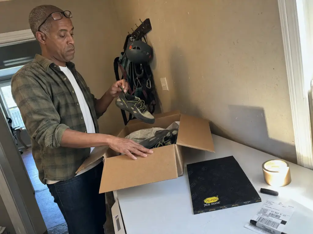 Packing climbing shoes into a shipping box for a resole, next to a sheet of Vibram XS Edge rubber