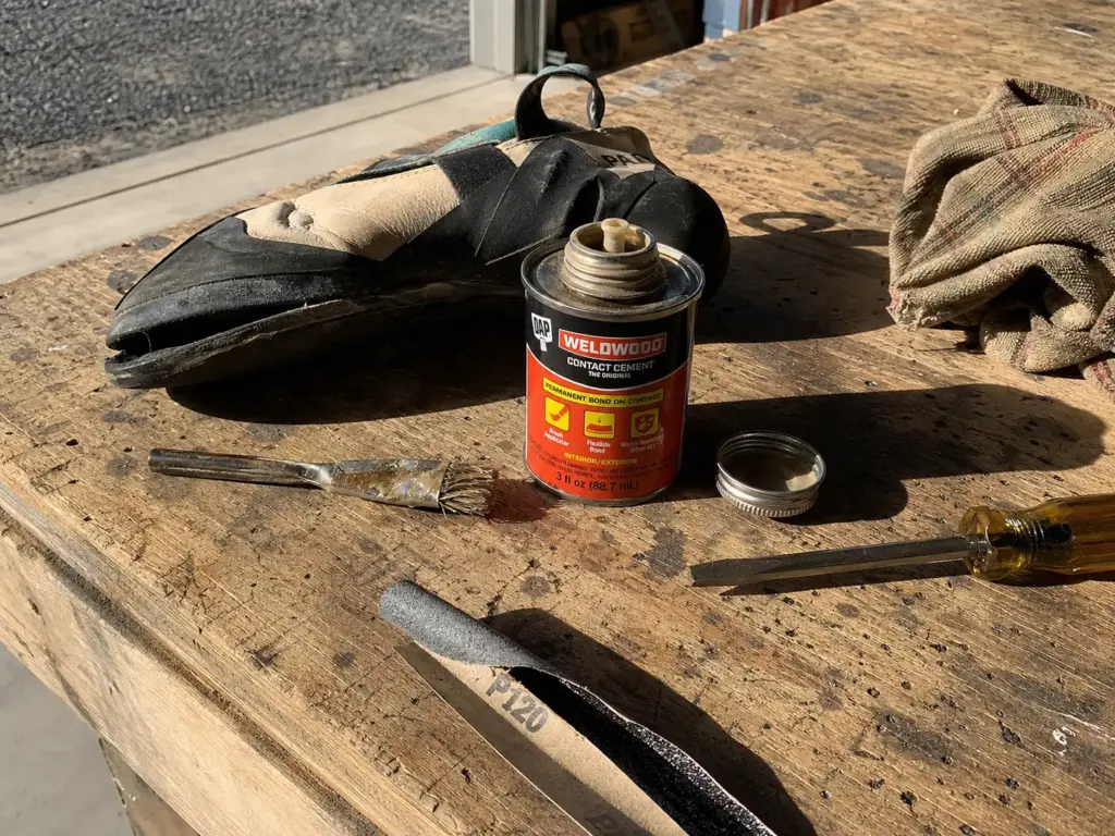 Contact cement tube and shoe repair adhesives laid out on a workbench beside a climbing shoe
