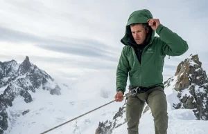 After 50 Alpine Climbs: The Layering System That Works Experienced alpinist pauses on a wind-scoured alpine ridgeline, adjusting down belay parka over Gore-Tex shell, high-altitude layering system in action