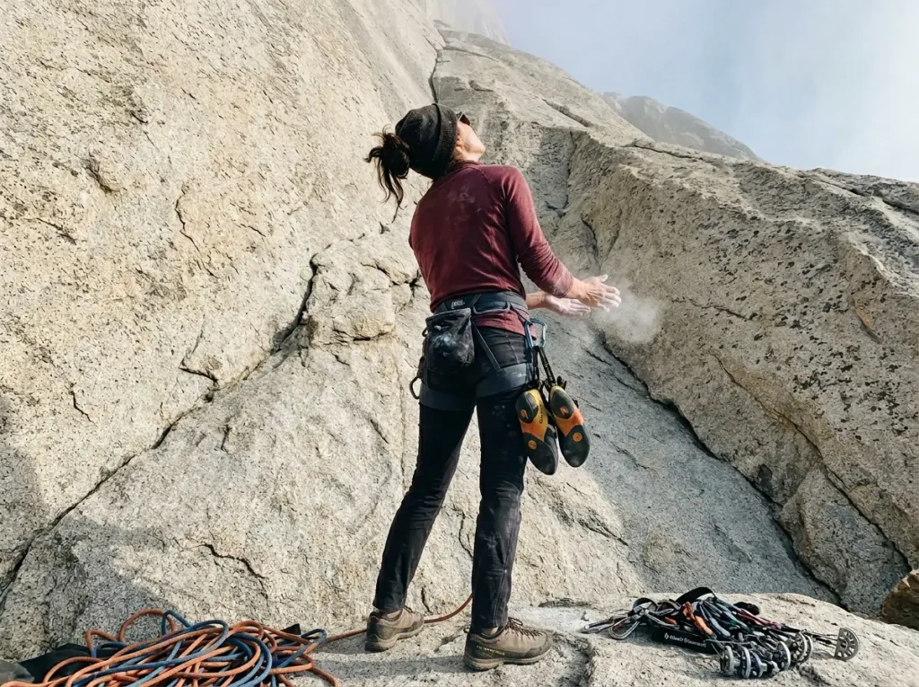 A climber chalking up at the base of a towering granite wall, looking up at a big-wall free climbing route