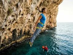 How to Start Deep Water Soloing Without Getting Hurt Climber falling feet-first into deep water below Mediterranean sea cliff during deep water soloing