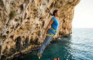 How to Start Deep Water Soloing Without Getting Hurt Climber falling feet-first into deep water below Mediterranean sea cliff during deep water soloing