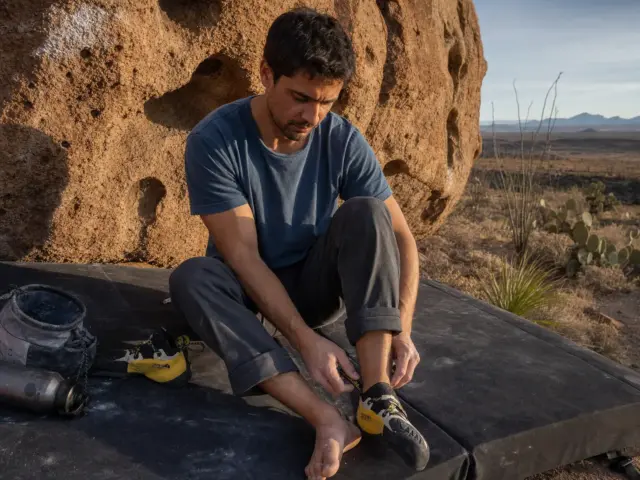 0-best-aggressive-climbing-shoes-hueco-tanks-hero Climber lacing aggressive climbing shoes on a crash pad at Hueco Tanks before a boulder attempt