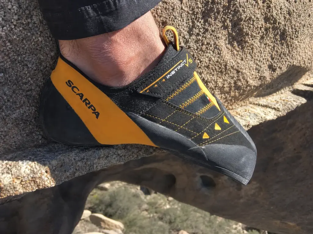 Close-up of a climbing shoe toe edging on a thin rock edge showing sole rubber thickness