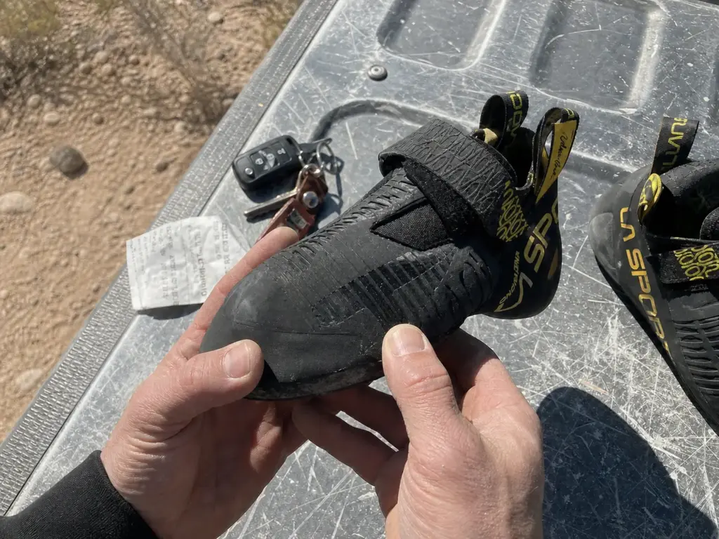 Hands inspecting a worn toe rand on an aggressive climbing shoe to decide on a resole