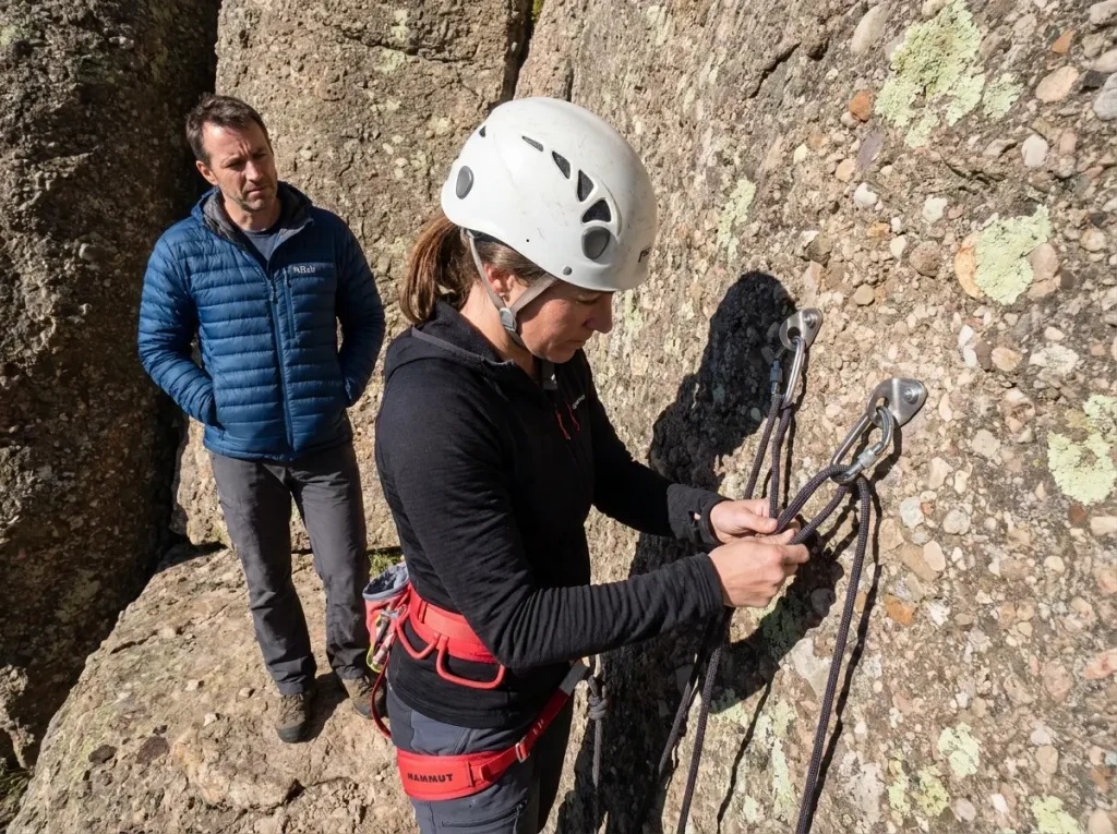 AMGA certified rock guide checking anchor systems on a single-pitch wall with client watching