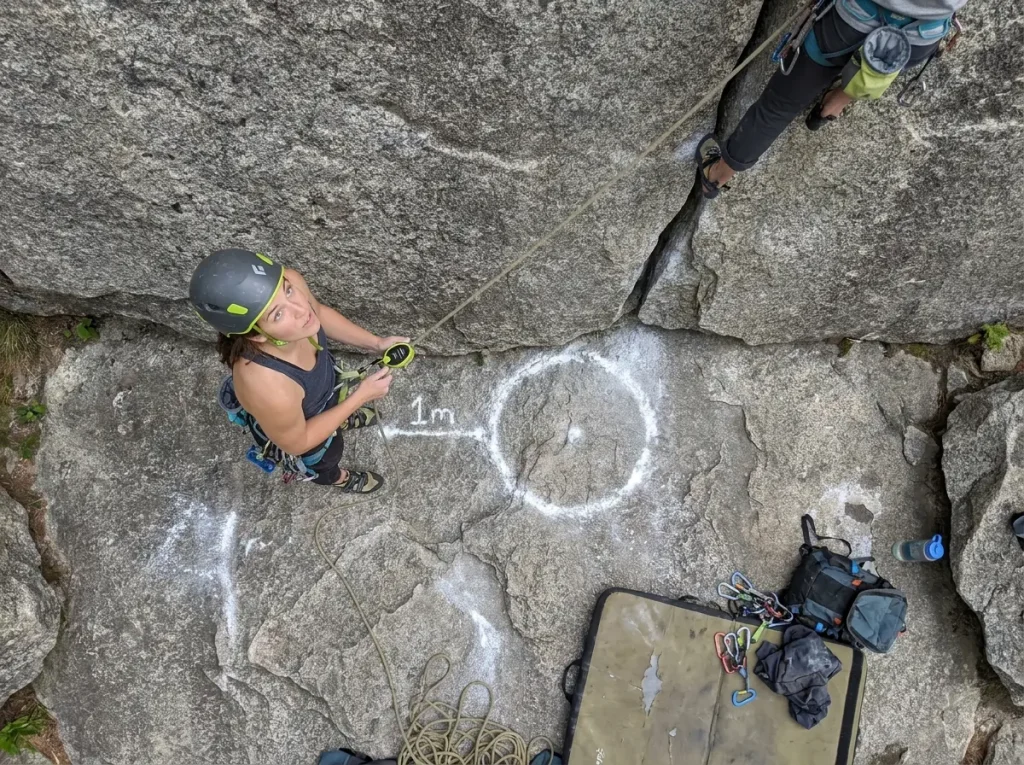 Outdoor belayer standing correct 1-meter distance from wall base on granite trad route