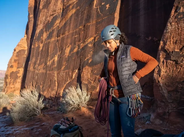 best-winter-climbing-destinations-hero Climber layering up at base of warm desert sandstone wall in winter morning light