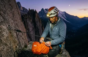 Why Staying Warm Is Only Half Your Bivouac Problem Climber in headlamp light setting up emergency bivy sack on granite ledge at dusk, alpine backdrop