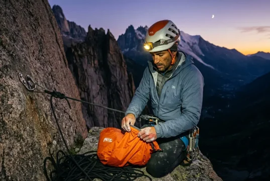 Why Staying Warm Is Only Half Your Bivouac Problem Climber in headlamp light setting up emergency bivy sack on granite ledge at dusk, alpine backdrop