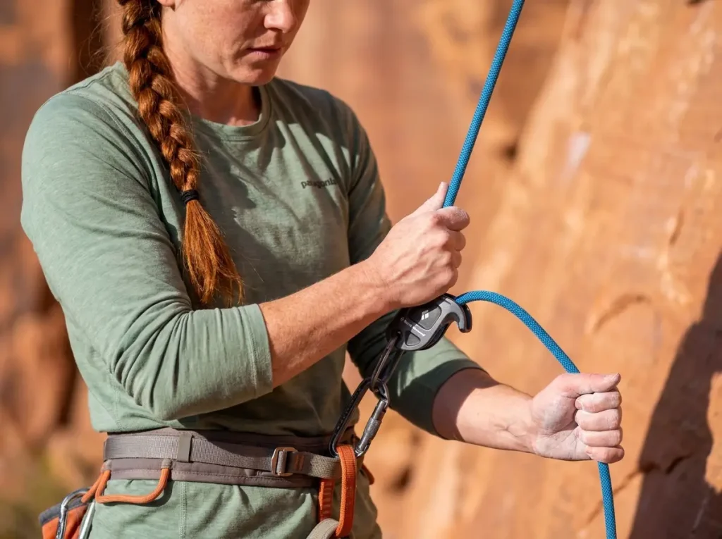 Climber demonstrating correct brake hand position below an ATC device while belaying outdoors