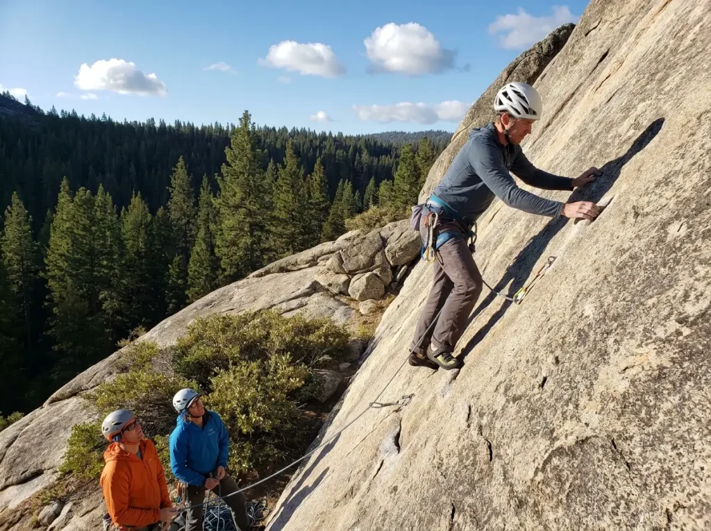 Guide leading a two-person client group on moderate granite multi-pitch, rope trailing below