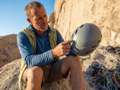 How to Inspect a Climbing Helmet Before It Fails You Climber holding a Petzl climbing helmet up to light for inspection at a granite crag