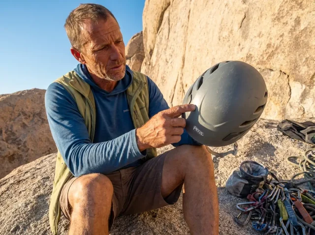 climbing-helmet-inspection-how-to-check-before-climbing-hero Climber holding a Petzl climbing helmet up to light for inspection at a granite crag