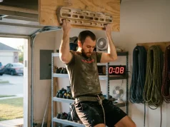 Dead Hang Benefits and How to Build a Progression Climber doing active dead hang on Metolius hangboard in home training space with focused expression